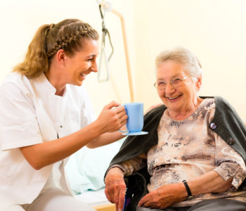 nurse giving cup of water to elder woman